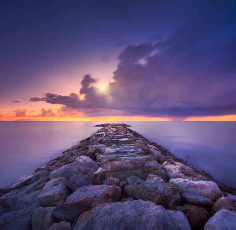 Rocky jetty and thunderstorm on the horizon. Marina di Cecina beach, Tuscany, Italy.
